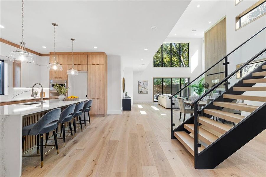 Kitchen with hanging light fixtures, sink, light hardwood / wood-style flooring, light stone countertops, and a towering ceiling