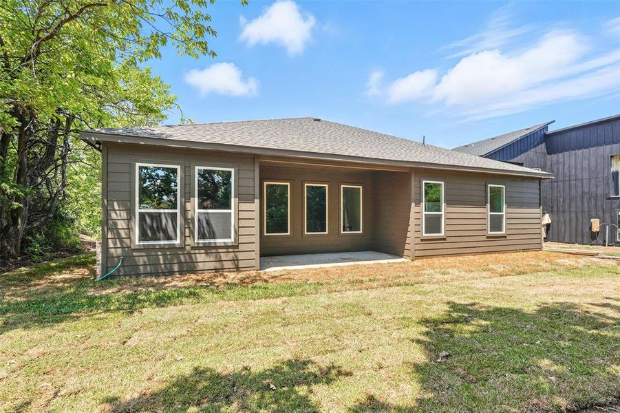 Back of property featuring a patio area, a lawn, and a shingled roof Back of property featuring a patio area, a lawn, and a shingled roof