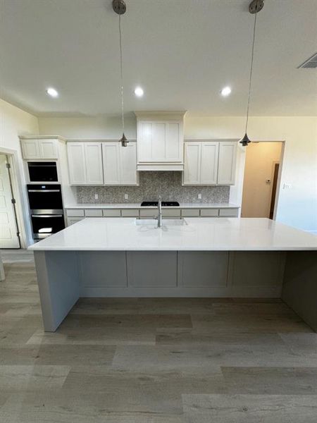 Kitchen featuring light hardwood / wood-style floors, decorative backsplash, a spacious island, and white cabinets