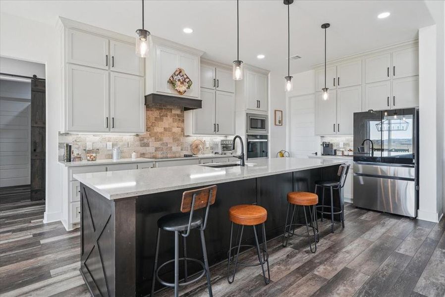 Kitchen featuring backsplash, stainless steel appliances, a barn door, a kitchen bar, and light stone countertops