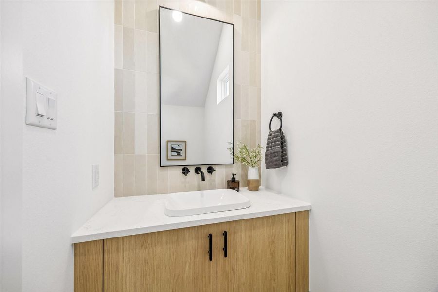 Warm wood cabinetry, full height designer tile, quartz surfaces, and a sculptural vessel sink create a powder bath that feels intentionally curated.