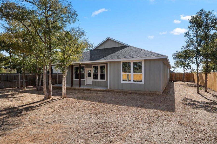 Rear view of property featuring a shingled roof, a patio area, a fenced backyard, and board and batten siding