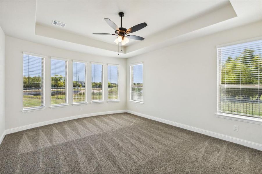 Empty room with ceiling fan, carpet flooring, and a tray ceiling