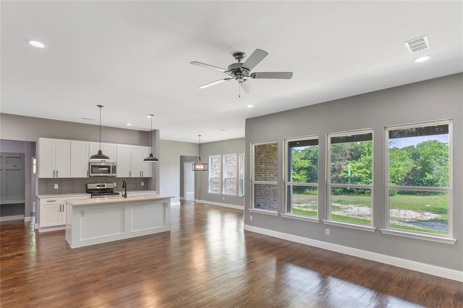 Kitchen featuring appliances with stainless steel finishes, white cabinetry, an island with sink, decorative backsplash, and hanging light fixtures