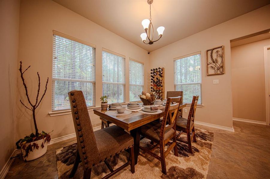 This inviting dining area features a wooden table set for six, with plush chairs and a cozy rug. Large windows let in natural light, and a stylish chandelier adds elegance. The neutral walls are complemented by tasteful decor, including a wine rack and artwork.