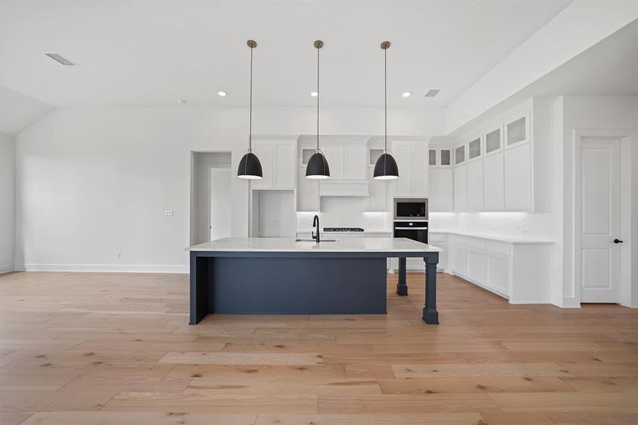 Kitchen with white cabinetry, decorative light fixtures, an island with sink, a breakfast bar area, and light wood finished floors Kitchen with white cabinetry, decorative light fixtures, an island with sink, a breakfast bar area, and light wood finished floors