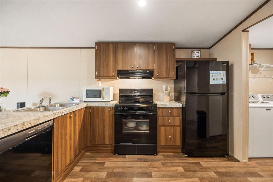 Kitchen featuring wood-finish cabinetry, black appliances including a refrigerator and range, a double basin sink, and wood-look flooring Kitchen featuring wood-finish cabinetry, black appliances including a refrigerator and range, a double basin sink, and wood-look flooring