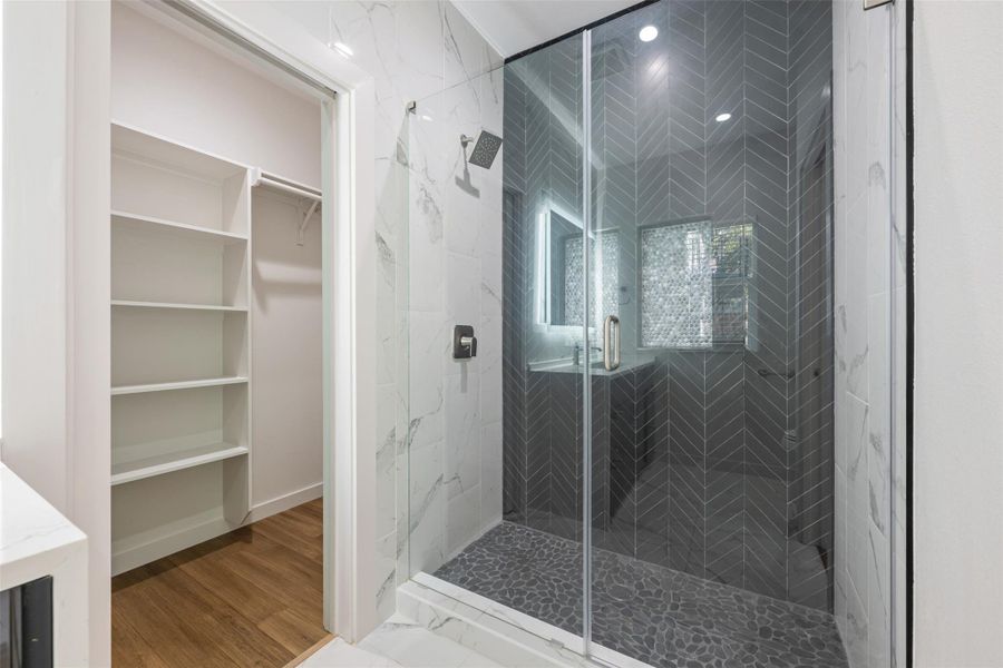 Bathroom with a marble finish shower, a walk in closet, and wood finished floors