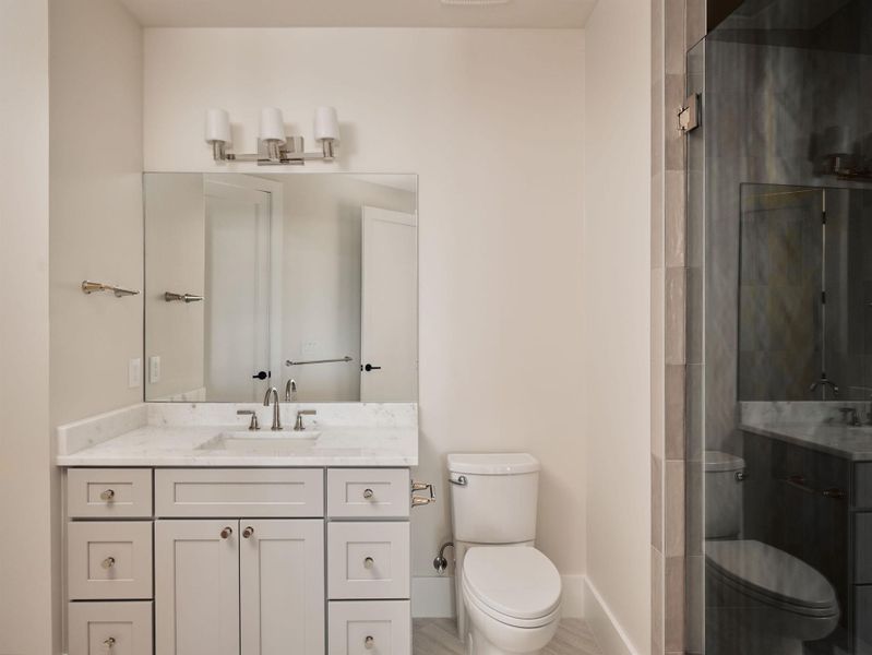 Modern bath with marble-look counters, ample storage, and a seamless glass shower enclosure. Modern bath with marble-look counters, ample storage, and a seamless glass shower enclosure.