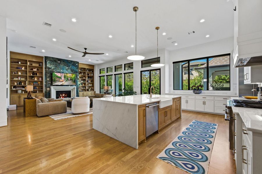 Chef’s kitchen with oversized waterfall island, custom cabinetry, and premium appliances opens to a spacious living area with fireplace and built-ins. Highlights include wide-plank hardwood floors, recessed lighting, and refined finish details throughout.