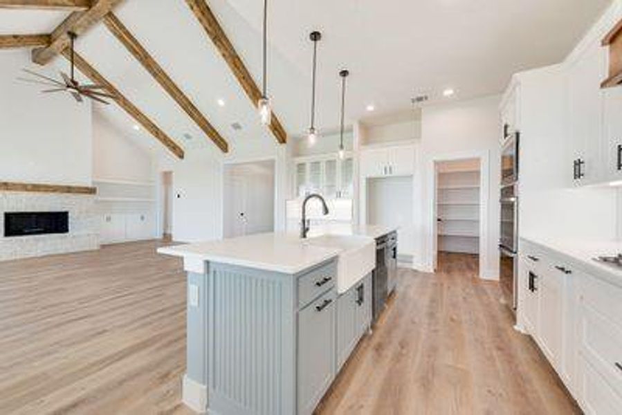 Kitchen featuring a large fireplace, lofted ceiling with beams, white cabinetry, decorative light fixtures, and a center island with sink