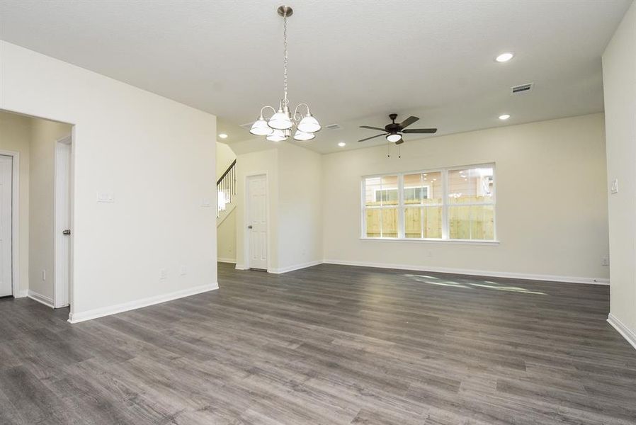 Spacious, empty room featuring wood flooring, white walls, modern lighting fixtures, and large windows with a backyard view.