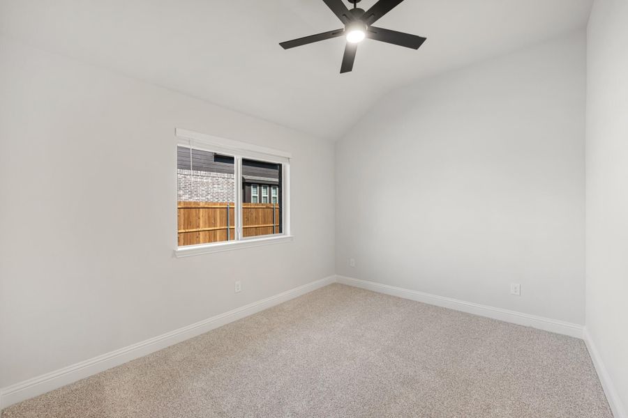 Empty bedroom with carpet flooring, black ceiling fan, and single window overlooking wood fence