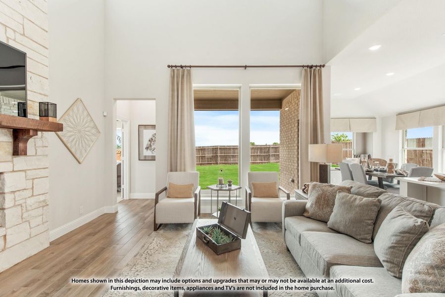 Living room with high ceilings, stone fireplace, hardwood floors, and large windows overlooking a backyard