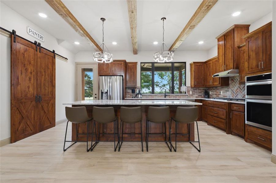 Spacious kitchen featuring an expansive island with seating, natural wood cabinetry, stainless steel appliances, and wood-finish flooring