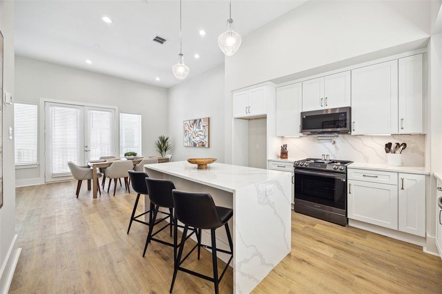 Gourmet kitchen features a waterfall quartz island with matching counters and backsplash. Sleek black toned appliances are all included! (Refrigerator will be installed soon.)