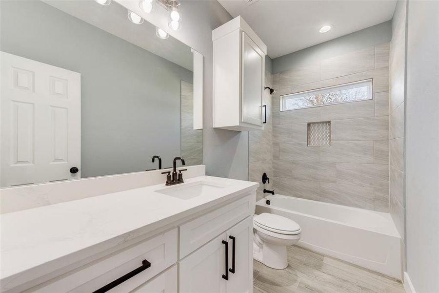 Full bathroom with hardwood / wood-style flooring, tiled shower / bath, vanity, and toilet