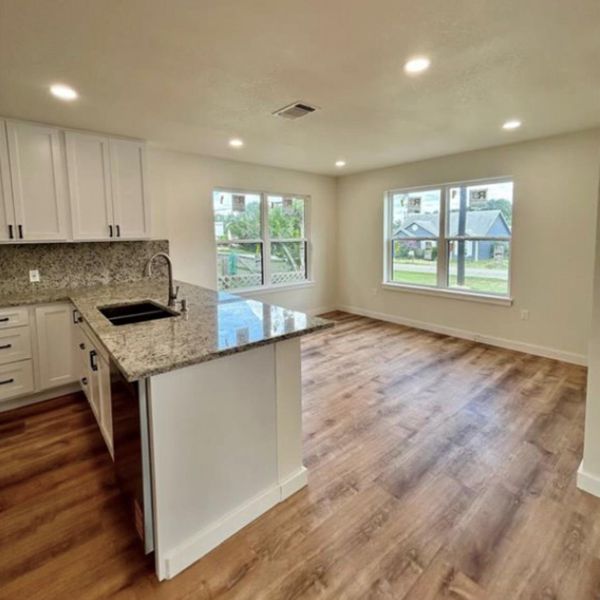 Modern kitchen with granite island and light-colored cabinetry opens to a naturally illuminated space.