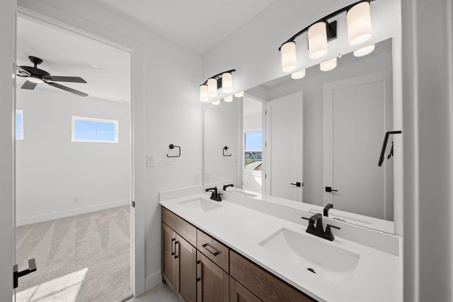 Bathroom featuring double vanity, healthy amount of natural light, light carpet, and a ceiling fan