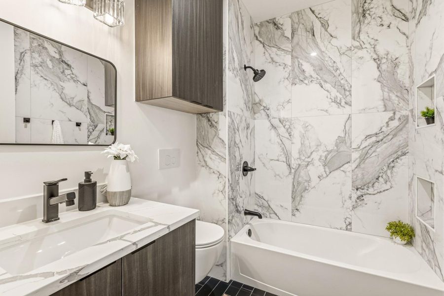 Bathroom featuring a built-in bathtub with black fixtures, large-format veined wall tiles, a built-in shower niche, a wood-finish vanity with a white countertop, and a rectangular mirror
