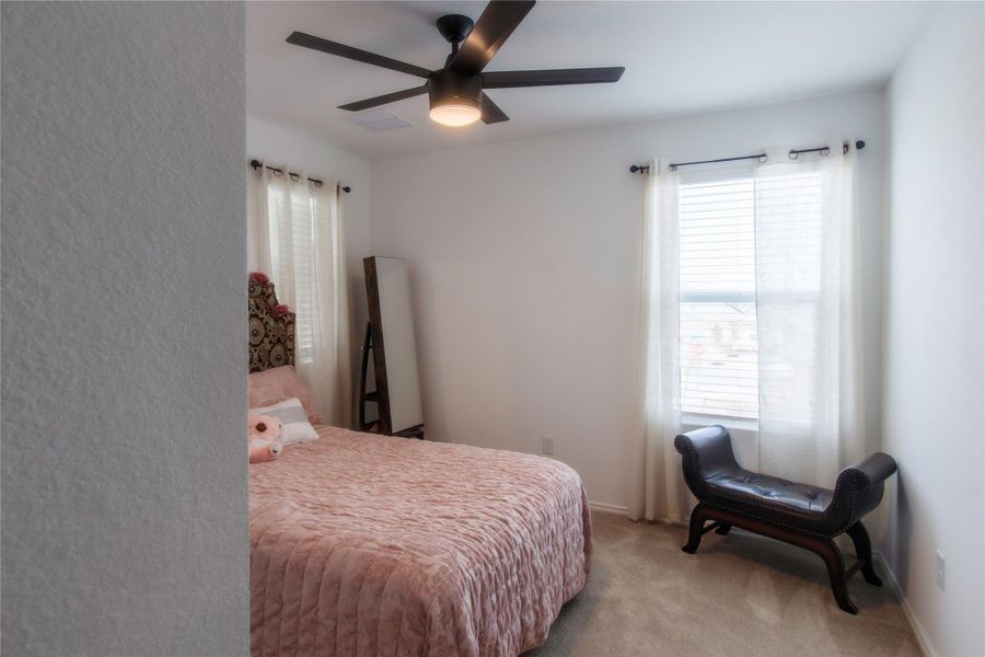 Generous secondary bedroom filled with natural light, neutral carpet, and a ceiling fan—perfect for comfort and versatility.