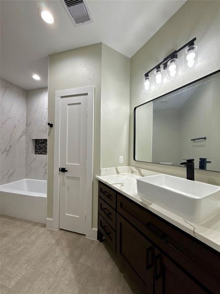 This modern bathroom features a spacious vanity with a vessel sink, sleek black fixtures, and ample storage. The room includes a large mirror with stylish lighting above. A marble-tiled shower and tub area adds elegance, complemented by neutral tones throughout. This modern bathroom features a spacious vanity with a vessel sink, sleek black fixtures, and ample storage. The room includes a large mirror with stylish lighting above. A marble-tiled shower and tub area adds elegance, complemented by neutral tones throughout.