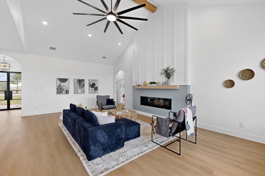 Living area with arched walkways, beam ceiling, a ceiling fan, light wood finished floors, and high vaulted ceiling