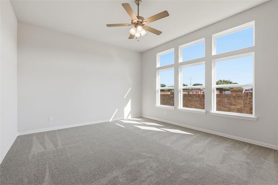 Spacious room featuring a vaulted ceiling with a ceiling fan, plush grey carpeting, and a wall of six large windows with white trim