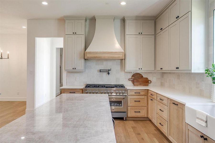 Kitchen featuring tasteful backsplash, high end stove, premium range hood, light hardwood / wood-style floors, and light stone counters