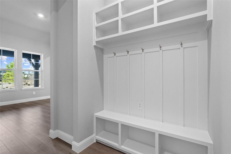 Step into this highly functional and stylish mudroom drop zone, an essential feature for a busy household. The space boasts custom-built white cabinetry and shelving, providing generous storage for coats, bags, and shoes. A comfortable built-in bench offers a convenient spot to sit, while three sleek hooks keep outerwear tidy and accessible.
