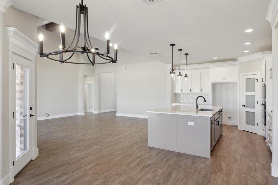 Kitchen featuring an island with sink, hanging light fixtures, a chandelier, white cabinetry, and dark hardwood / wood-style flooring