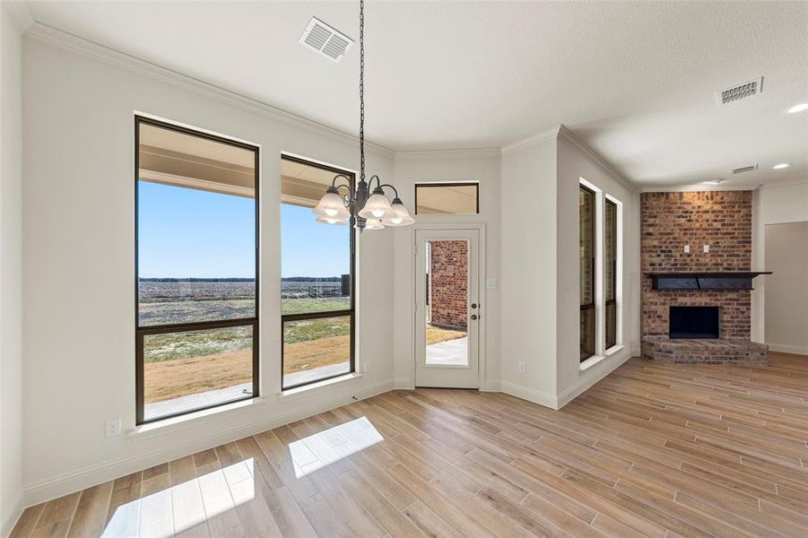 Unfurnished dining area featuring wood tiled floors, a chandelier, crown molding, and a brick fireplace Unfurnished dining area featuring wood tiled floors, a chandelier, crown molding, and a brick fireplace
