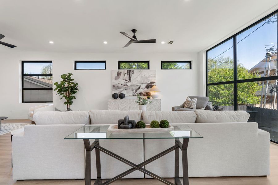 Clerestory windows run along the upper wall while a full-height black-framed window anchors the side — the combined light pours into the main family room throughout the day without sacrificing wall space below. The open plan connects seamlessly to the dining room and kitchen from here.