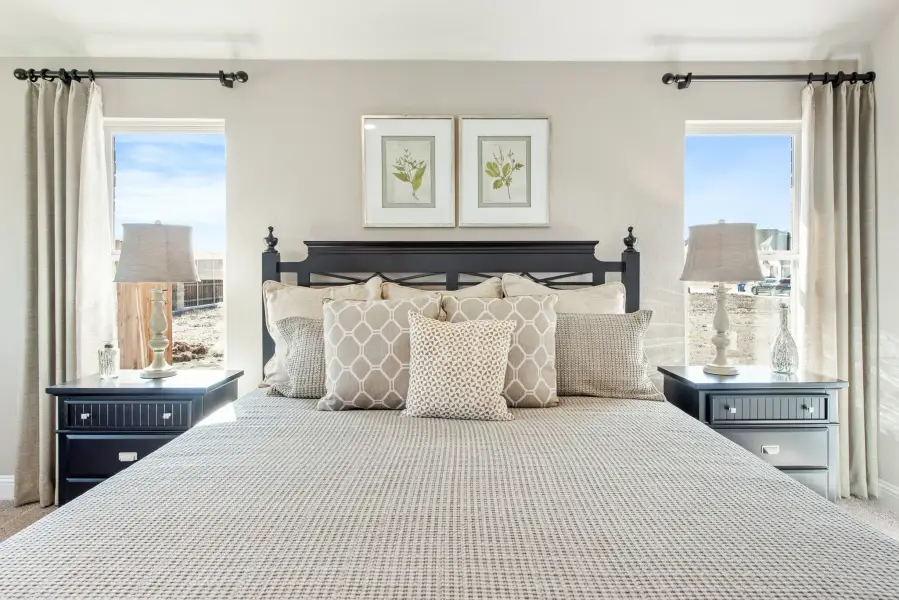 Bedroom with king bed, dark wood headboard, two nightstands, and windows with neutral drapes on each side