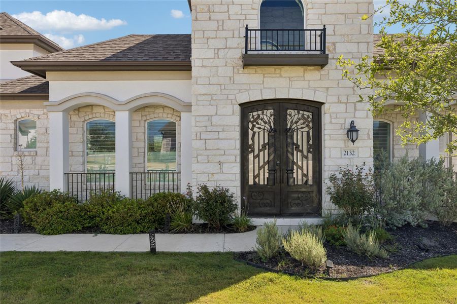 Ornate iron double doors welcome you to a grand facade of natural stone and lush landscaping.