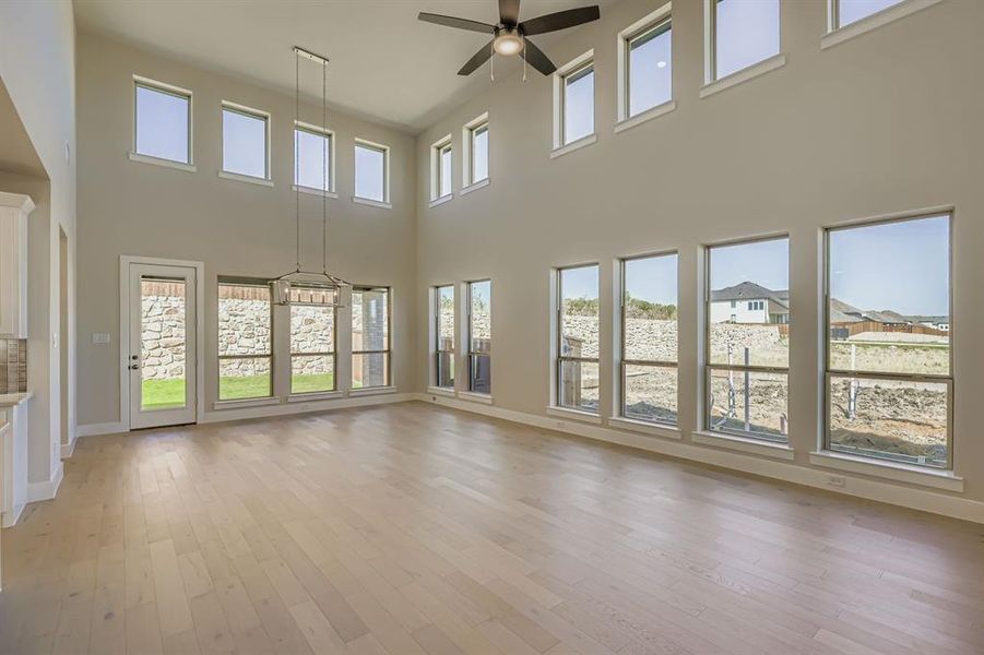 Unfurnished living room with light wood-style flooring, ceiling fan, and a towering ceiling