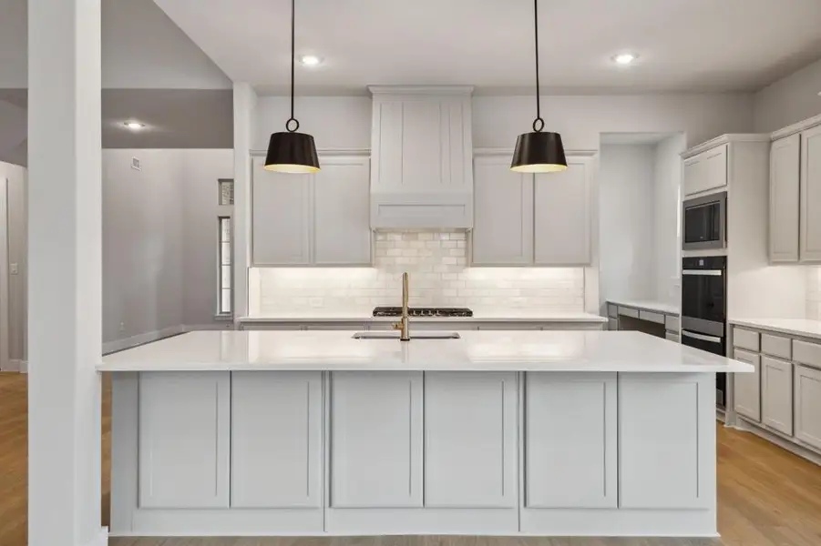 Kitchen featuring stainless steel appliances, tasteful backsplash, light countertops, light wood-style floors, and an island with sink