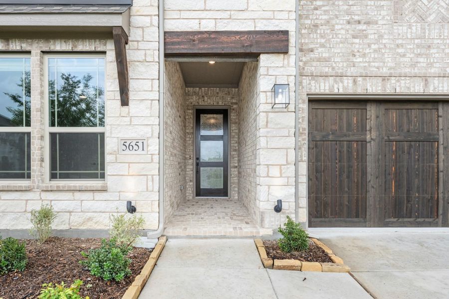 Stone and brick home exterior with covered front entry, dark wood garage door, and address number 5651 Stone and brick home exterior with covered front entry, dark wood garage door, and address number 5651