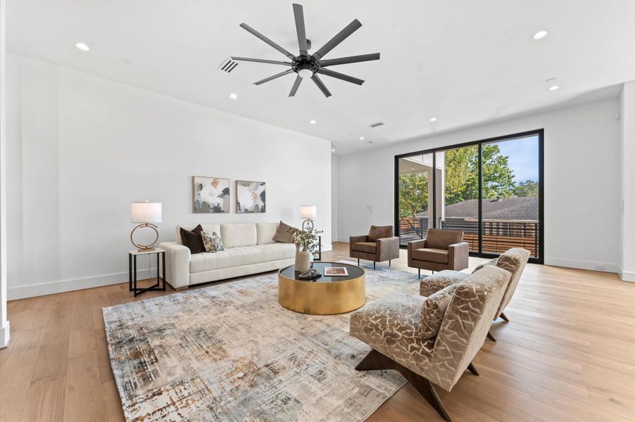 This spacious living room features modern decor with a neutral color palette, a large sliding door for natural light, and a ceiling fan. The open layout includes a cozy seating area, accent chairs, and stylish artwork, creating a welcoming atmosphere.