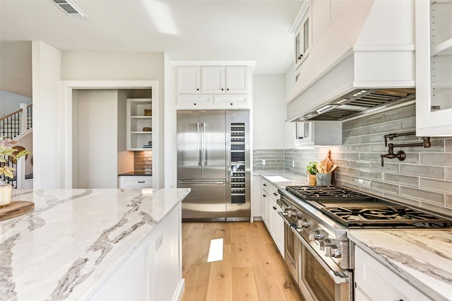 Sunlight pours across the kitchen and dining area, highlighting the elegant finishes and open concept design. The oversized island and full size wine fridge create the perfect setup for entertaining.