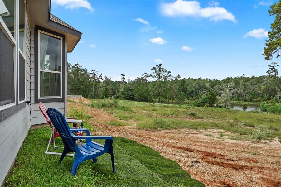 This photo shows the exterior back of the home with a view of the natural, serene setting, featuring nature and the neighborhood lake. There's a space with outdoor chairs, suggesting a spot for relaxation and enjoying the scenery.  Seller is regrading and putting in sod.