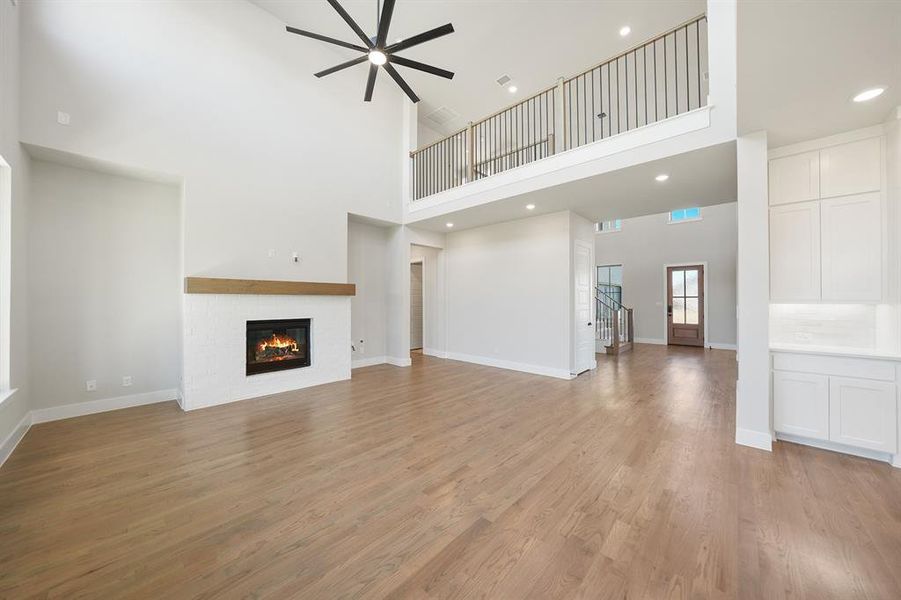 Unfurnished living room featuring a glass covered fireplace, light wood finished floors, recessed lighting, a towering ceiling, and ceiling fan Unfurnished living room featuring a glass covered fireplace, light wood finished floors, recessed lighting, a towering ceiling, and ceiling fan