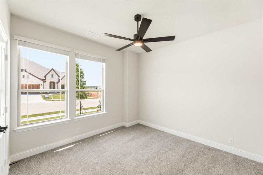Empty bedroom with carpet flooring, black ceiling fan, and two windows with neighborhood view