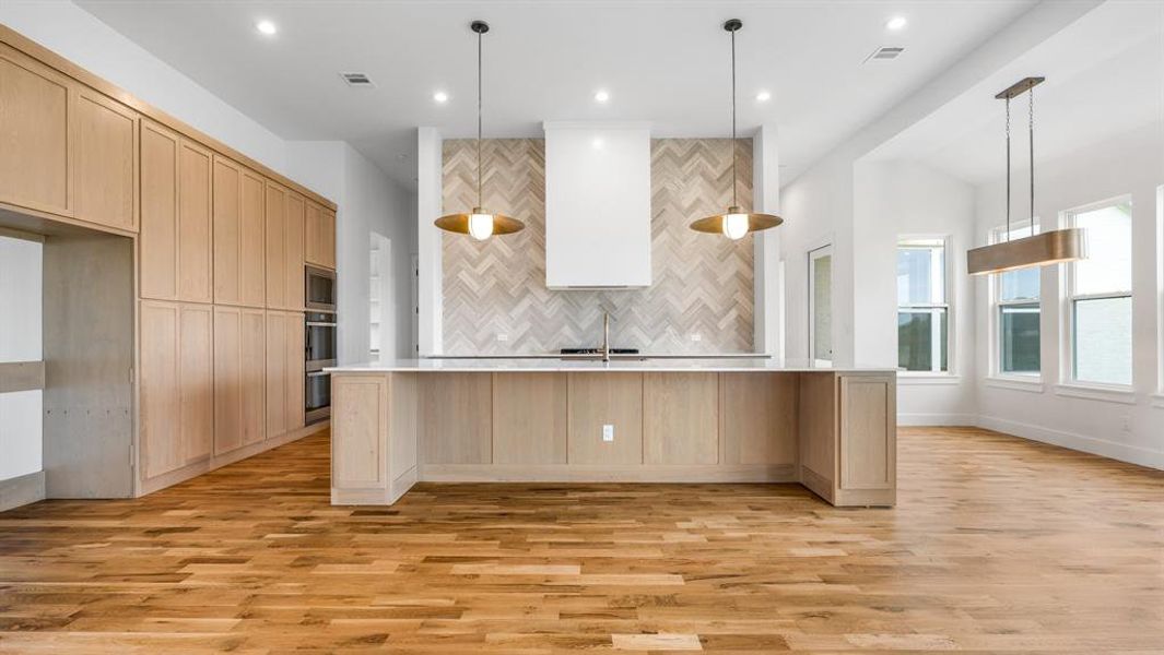 Kitchen with pendant lighting, a kitchen island with sink, light hardwood / wood-style floors, and light brown cabinets