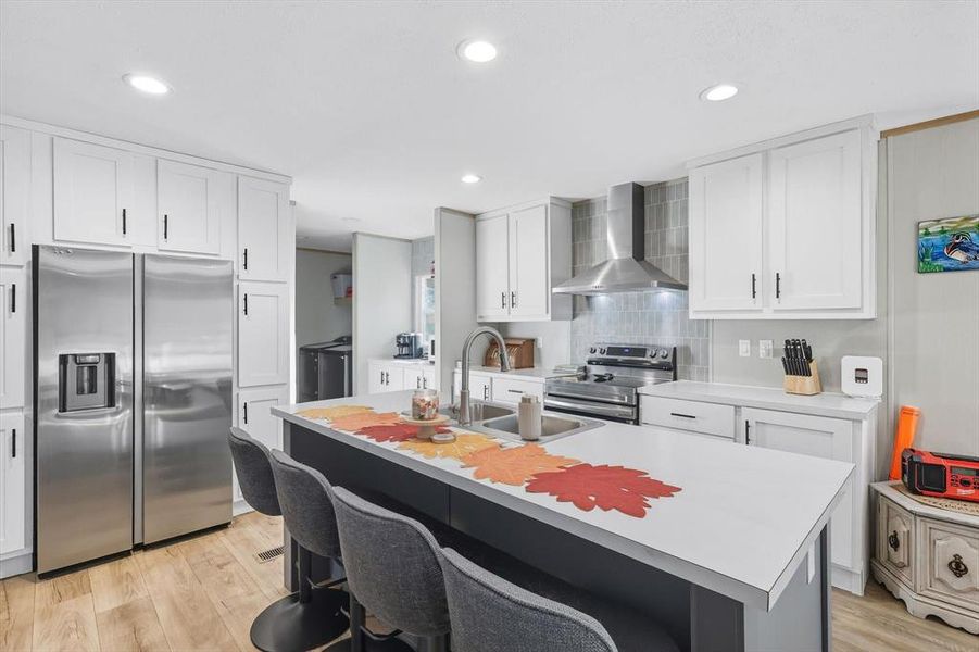 Kitchen with stainless steel appliances, light countertops, a breakfast bar, white cabinetry, and recessed lighting Kitchen with stainless steel appliances, light countertops, a breakfast bar, white cabinetry, and recessed lighting