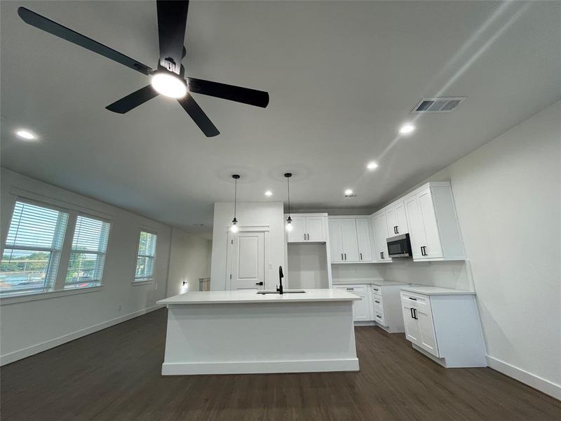 Kitchen with dark wood-style floors, white cabinetry, a center island with sink, recessed lighting, and decorative light fixtures