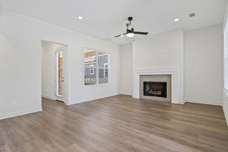 Spacious living area featuring wood-finish flooring, a contemporary ceiling fan, recessed lighting, a fireplace with a stone surround and white mantel, and a glass-paneled exterior door