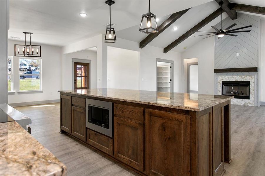 Kitchen with pendant lighting, stainless steel microwave, lofted ceiling with beams, a fireplace, and light hardwood / wood-style floors