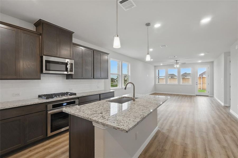 Kitchen featuring stainless steel appliances, light wood-style floors, decorative backsplash, dark brown cabinetry, and hanging light fixtures Kitchen featuring stainless steel appliances, light wood-style floors, decorative backsplash, dark brown cabinetry, and hanging light fixtures