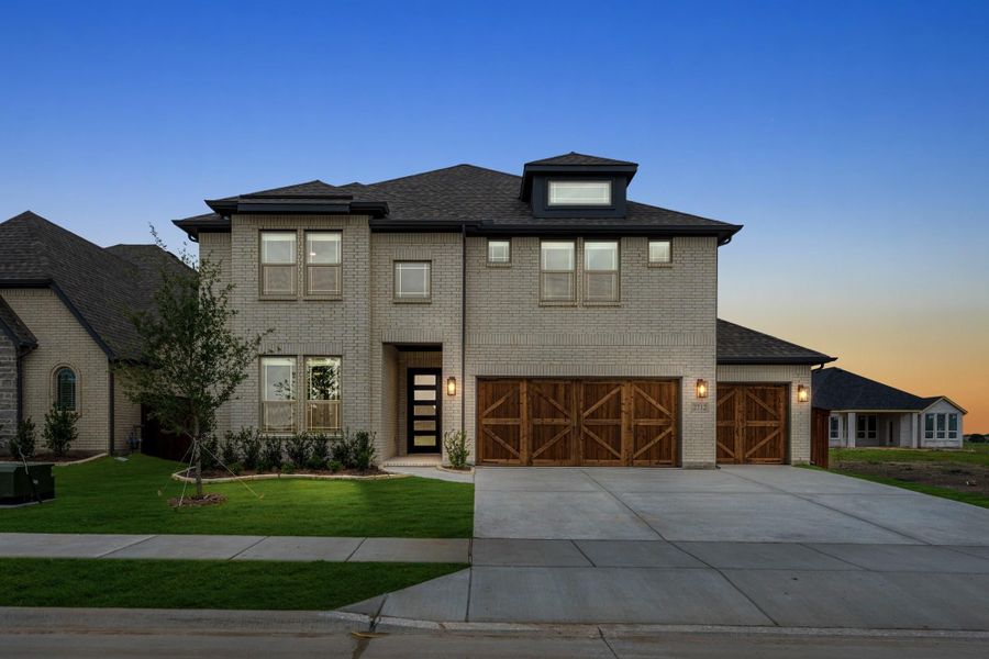 Two-story brick home with three-car garage, wood garage doors, and front lawn at dusk